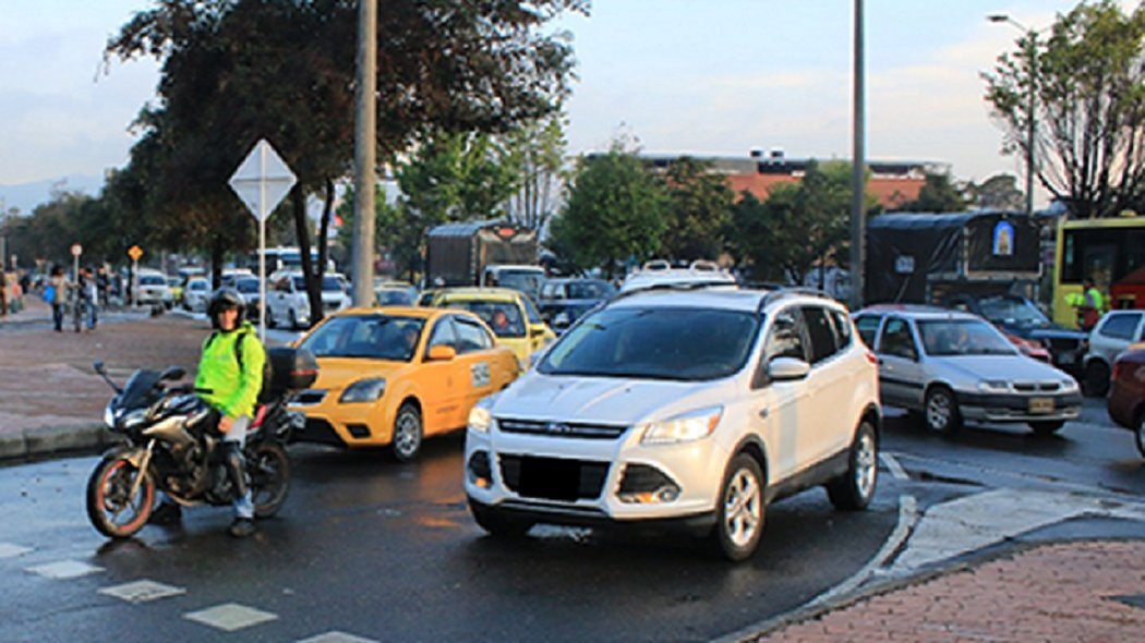 Taxis, una motocicleta y carros particulares circulando en una vía urbana